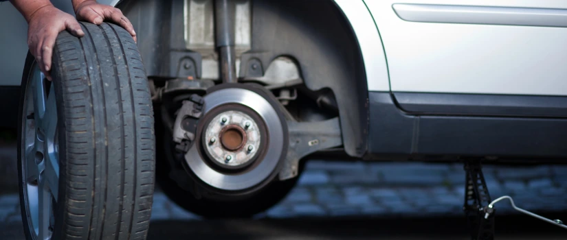 Automonteur wisselt winterbanden naar zomerbanden bij een auto op een krik, met zichtbare remschijf